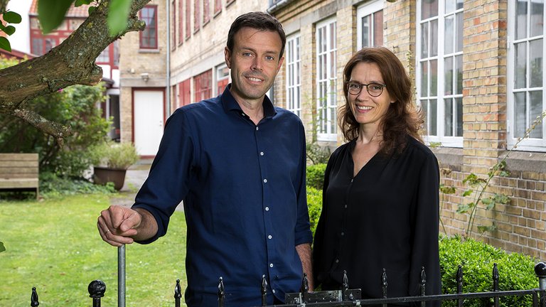 Par står foran gårdmiljø ved deres lejelejlighed i centrum af Odense