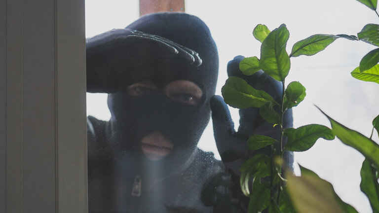 maskeret mand ser ind gennem vindue i bolig