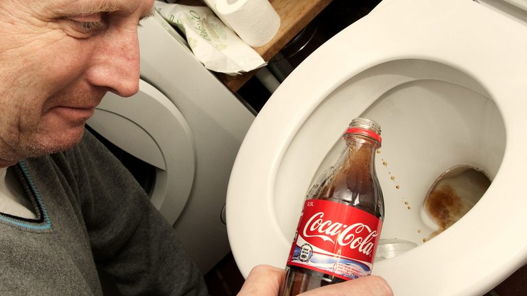 mand hælder cola ned i toilettet, hvor der er rust i