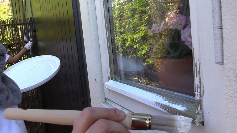 Maling af udendørs træværk på et vindue med malerpensel