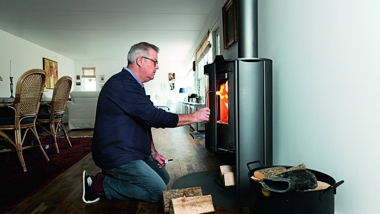 John Groser lukker glaslågen på sin brændeovn efter at have puttet brænde i den