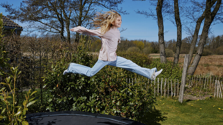 Ung pige hopper på trampolin i haven