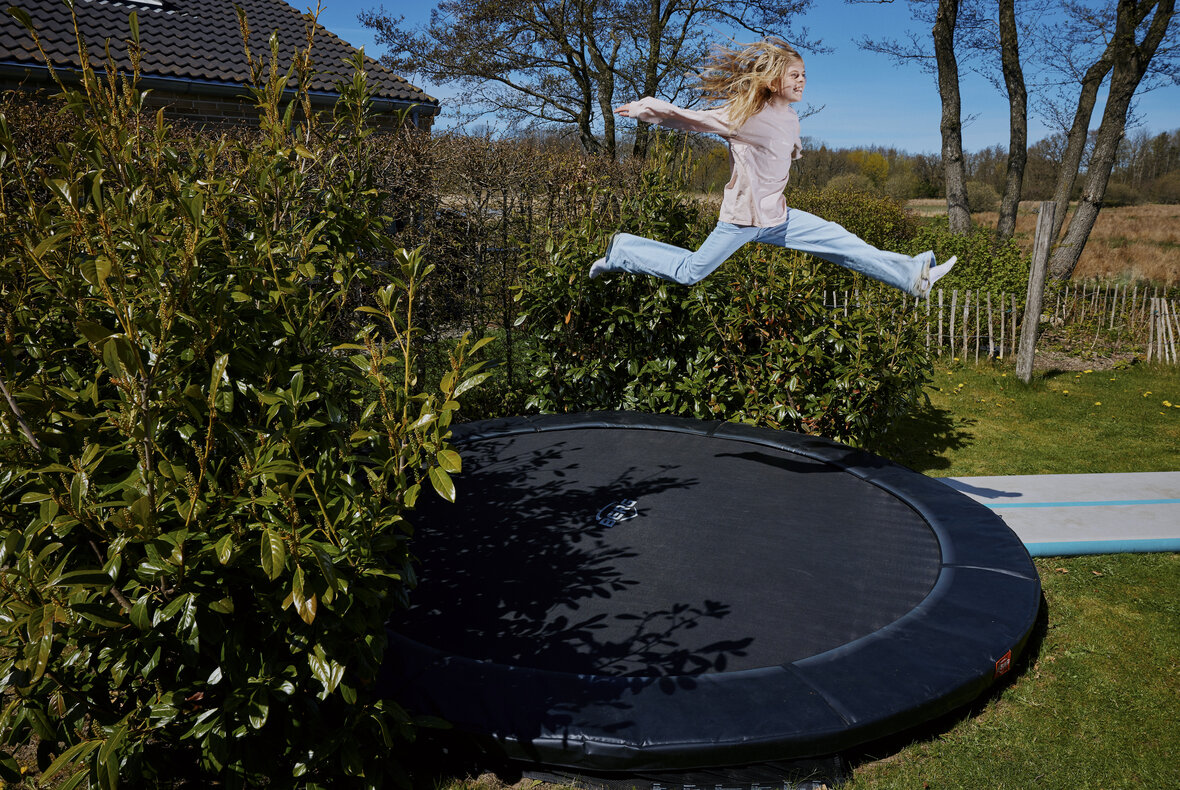 Ung pige hopper på trampolin i haven