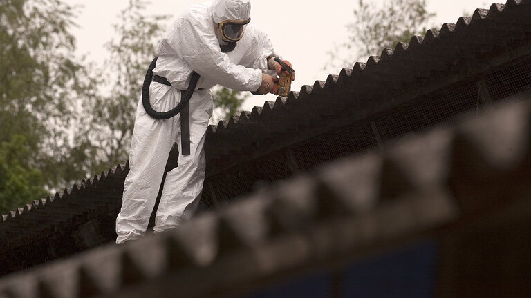 Mand i beskyttelsesudstyr fjerner asbesttag