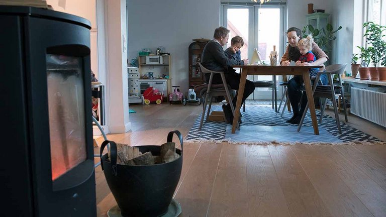 Familien Reifling Dieckmann sidder ved spisebord med brændeovn i forgrunden og radiator bagved