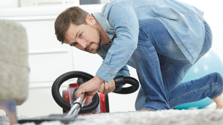mand støvsuger gulvtæppe foran sofa