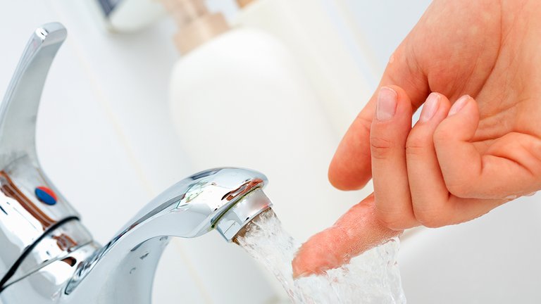 Finger mærker temperaturen på det løbende vand fra den kolde hane