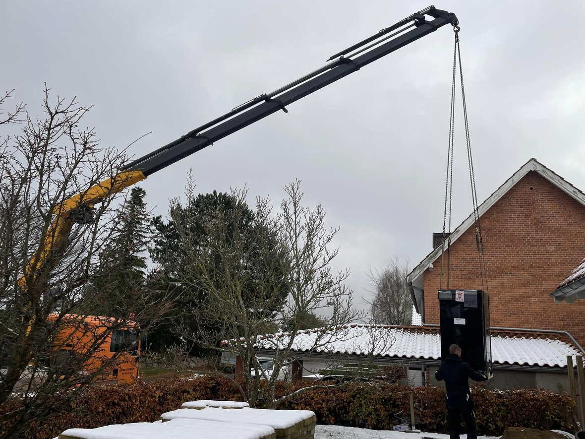 indedel af varmepumpe hejses hen til hus, hvor der ligger sne