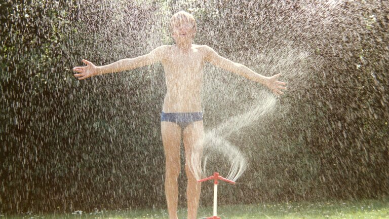 havevander på græsplæne sprøjter vand på dreng i badebukser