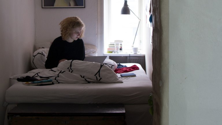 Kvinde sidder i seng i egen lejlighed
