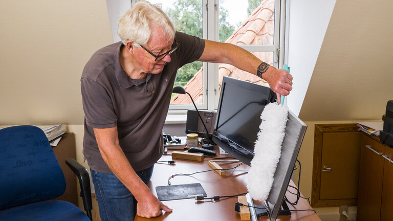 mand fjerner støv fra skærm med støvkost