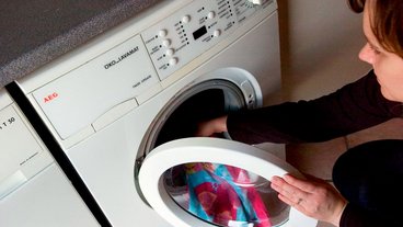 En kvinde lægger et farvet håndklædeind i en vaskemaskine.