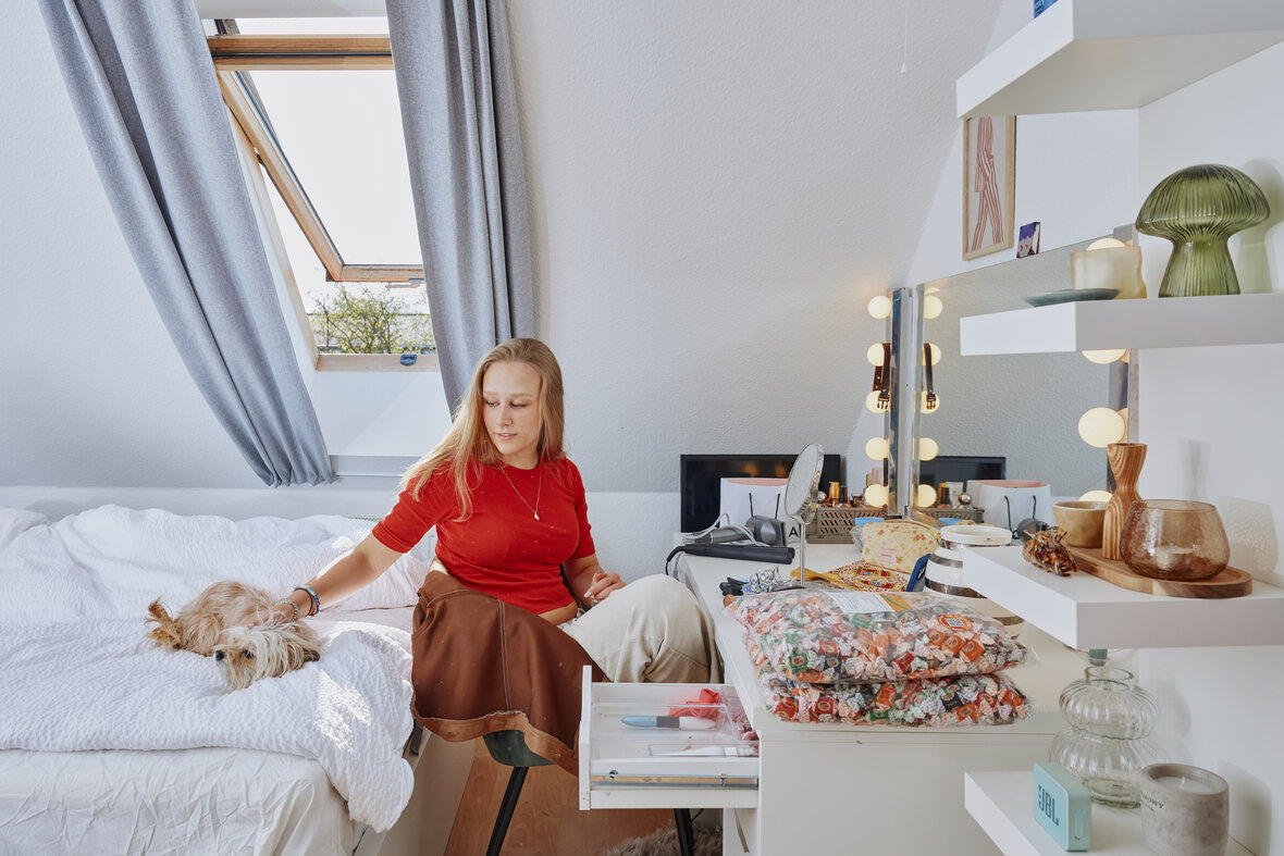 Ung pige sidder ved sit sminkebord, med sin lille hund ved siden af i sengen