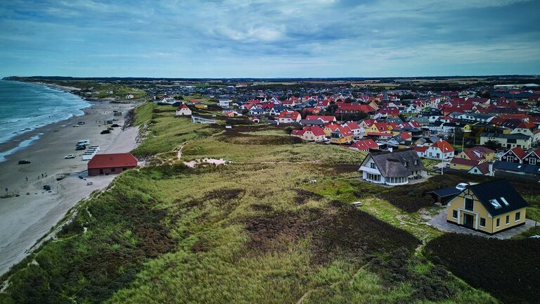 Sommerhuset ligger oppe på klitterne, og i baggrunden ses byen Løkken.