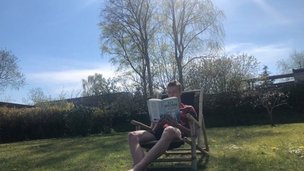 ung mand sidder i skygge i haven og læser da naboens høje træet kaster skygge i haven