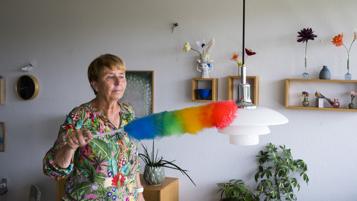 Kvinde fjerner støv fra lampe med støvkost