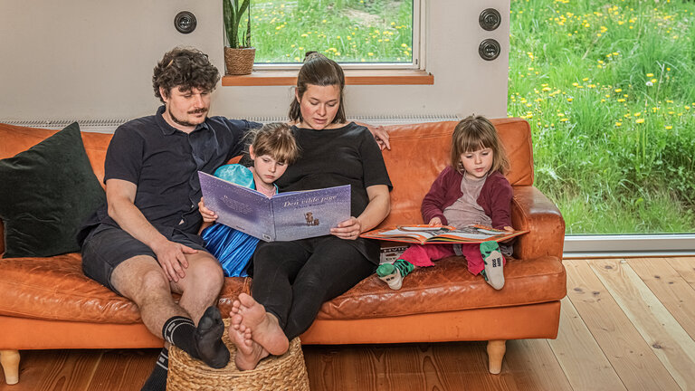 Elvira og Kasper Bergman-Coates i deres sofa sammen med deres børn i deres mikrohus på Djursæand