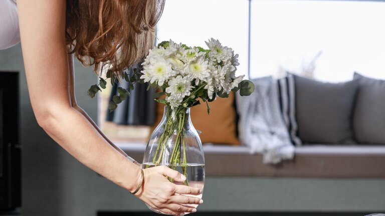 kvinde stiller glasvase med blomster på bord