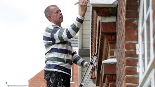 Boligejer står på en stige og maler vinduer på sin murermestervilla.