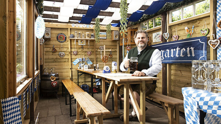 Kenneth Sørensen med stort ølkrus i hånden i sin carport, der er bygget om til ølstue, hvor der kan holdes oktoberfest