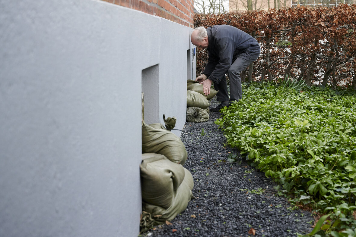 mand lægger sandsække foran kældervinduer