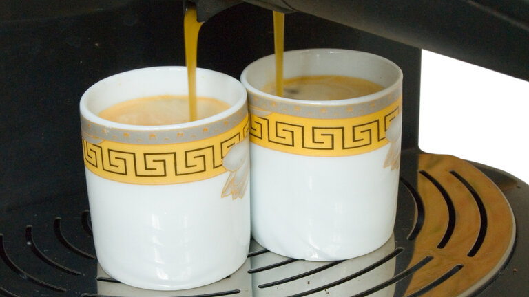 To kopper kaffe bliver lavet i en kaffemaskine