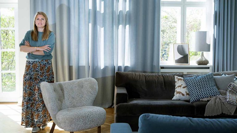 Camilla Lolk Nortvig foran vinduerne i stuen, hvor de gråblå, specialsyede gardiner hænger